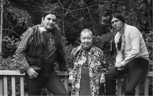 Schwarzweißfoto von Welskopf-Henrich mit den Native Americans Vernon Bellecourt und Dennis Banks, gegen einen Gartenzaun gelehnt