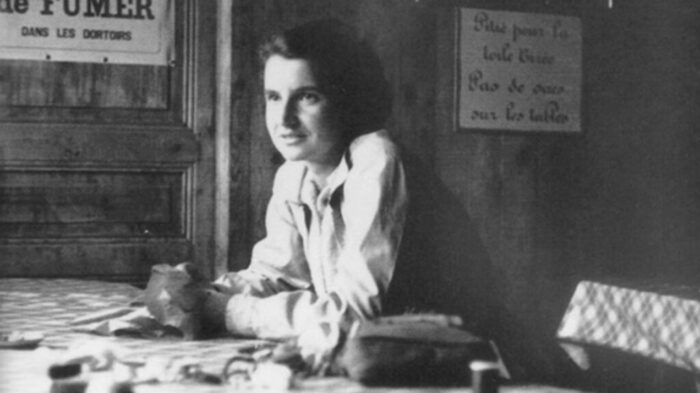 Schwarzweiß-Foto von Rosalind Franklin, die an einem Tisch in einer Berghütte sitzt
